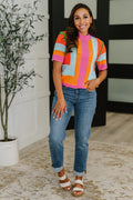 Model wearing drapey knit top tucked into trousers for an elevated look.
